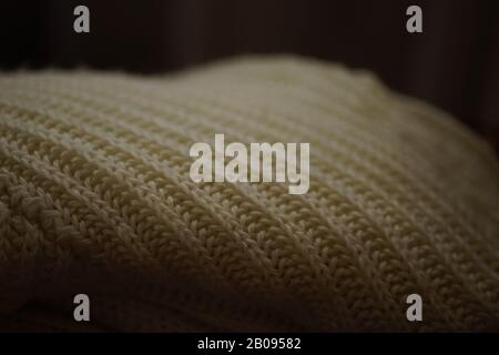 White knitted sweater lies on a sofa in dark room, close-up Stock Photo