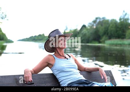 A woman in a cowboy hat, in nature. Near water. Stock Photo