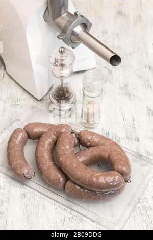 Raw beef sausages on wooden table close up. Meat grinder for cooking minced meat and spices to add spice to dish. Production of meat delicacies at hom Stock Photo