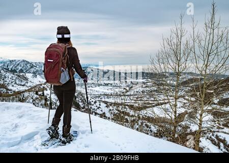 Hiker in the mountains walk on snowshoes. The girl on the edge of the hill look into the distance. View from the back. Winter mountain tourism. Kazakh Stock Photo