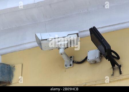 Surveillance camera mounted on tiled wall of house. Security concept, tracking system, monitoring and control. Stock photo for web and print with empty space for text. Stock Photo