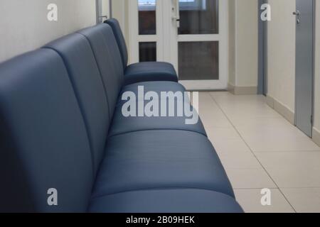Leather black sofa in an empty long corridor with doors. Concept of office furniture. Stock photo for web and print with empty space for text. Concept of office furniture. Stock Photo