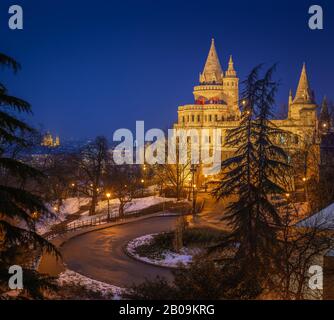 Budapest, Hungary - The north towers of the illuminated Fisherman's Bastion at blue hour with St. Stephen's Basilica and ferris wheel at background on Stock Photo