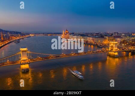 Budapest, Hungary - Aerial view of the famous illuminated Szechenyi Chain Bridge at blue hour with sightseeing boat on River Danube and Parliament at Stock Photo