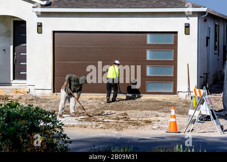 Construction workers with shovel and rake, leveling ground and preparing a driveway for pouring cement. Stock Photo