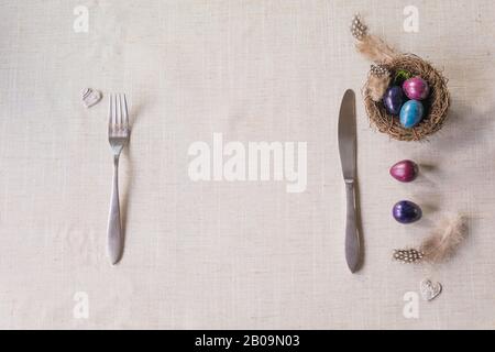 Easter festive spring table setting decoration, naturally dyed quail eggs in nests, feathers, wooden hearts, family dinner or breakfast concept Stock Photo