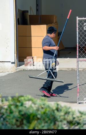 Construction worker raking freshly poured concrete mix on driveway in preparation for laying bricks. Stock Photo