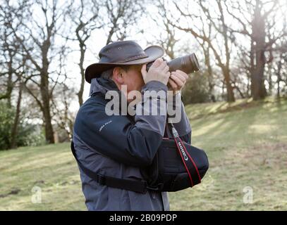 A male photographer wearing a hat holds a camera up to his face ready to take a photo. Stock Photo