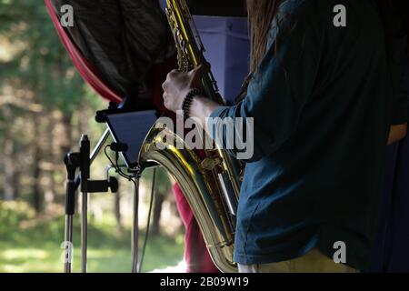 A soft focus midsection view of a saxophone player performing on stage at a multicultural music festival, with blurry trees and copy space to sides Stock Photo