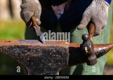 A closeup selective focus view of a metalworker using old fashioned tools during a demonstration at an artisan festival, shaping metal on anvil Stock Photo