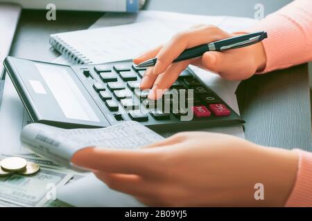The female accountant holds a cashier’s check in her hand and makes calculations on a calculator. Profit analysis, accounting of taxes, expenses