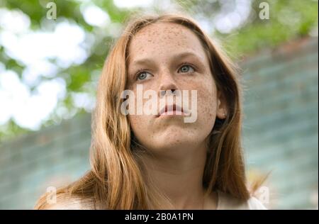 A pretty young teenage girl, with blue eyes, red hair, fair skin and freckles, looking off to the side, away from the camera. Stock Photo