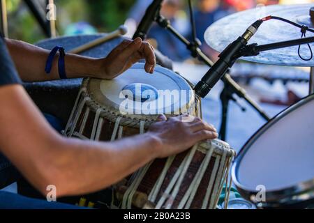 A close up selective focus cropped view of a man playing traditional folk drums on stage, at festival with mic stands and blurry arm in foreground Stock Photo
