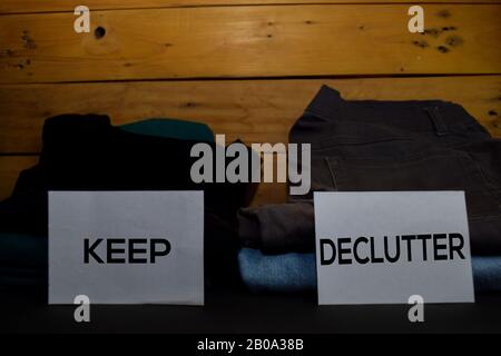 Keep and Declutter write on a sticky note between fashion clothes folded and stack isolated on wooden background. Stock Photo