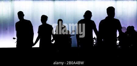 Silhouettes of people walking in the night , in front of modern building, in high contrast black and purple white Stock Photo