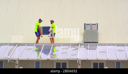 Two workers carry a new air con unit  across the top of a building Stock Photo