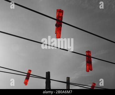 Bright red plastic pegs on a clothes line against a grey sky Stock Photo