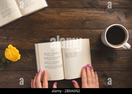 Female hands and opened book, on wooden background. Flat lay, top view, copy space. Stock Photo