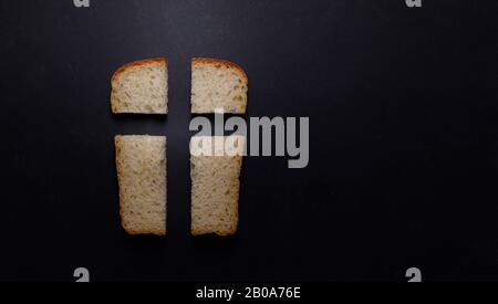Our daily bread, a metaphor and sign. Cross, Christian values, Christian religion concept. Bread in the form of a cross on a black background, top vie Stock Photo