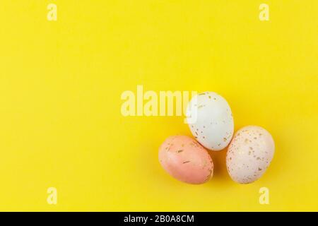 Creatively dyed decorative eggs in pastel colors decorated with gold leaf on yellow background, copy space. Happy Easter do it yourself concept. Flat Stock Photo
