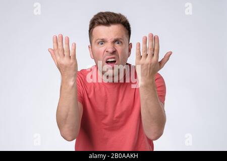 Furious, enraged man with grumpy grimace on his face,with mouth opened in shout, ready to argue. Studio shot Stock Photo