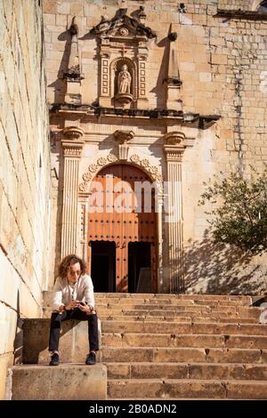 Man with iphone, sitted on staircase, outside baroque temple Stock Photo