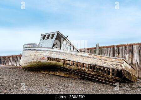 A wrecked boat on the shore next to an old wharf. The boat is in very poor shape and is falling apart. Low tide. Stock Photo