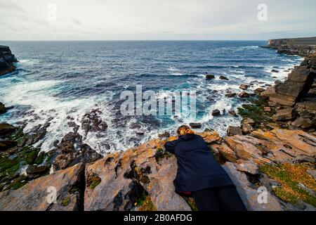 High angle view of a woman lying on a cliff overlooking the ocean Stock Photo