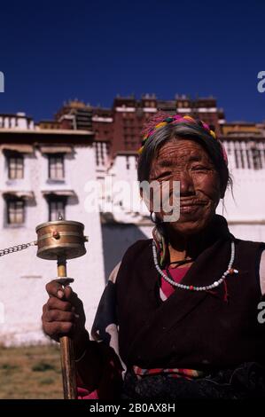 CHINA, TIBET, LHASA, WOMAN WITH PRAYER WHEEL, POTALA IN BACKGROUND Stock Photo