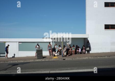 People waiting at a  Bondi Beach bus stop; white building cut against a blue sky on  a sunny day, on Campbell Parade, Sydney, Australia Stock Photo