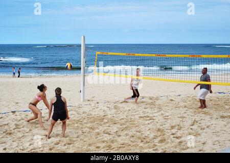 Four people playing beach volleyball for fun at Coogee beach a woman in a sports bikini is about to return the ball, summer days in Sydney, Australia Stock Photo