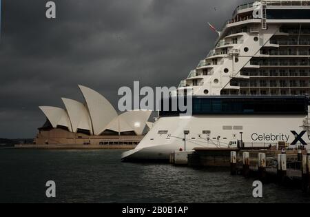 The Sydney Opera House dwarfed by a large cruise ship berthed at the overseas passenger terminal, white ship and 'sails' against a dark   stormy sky Stock Photo