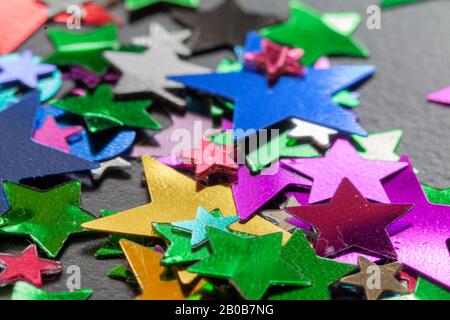 Party confetti multi colored stars and shaped close up scatted on a black table Stock Photo
