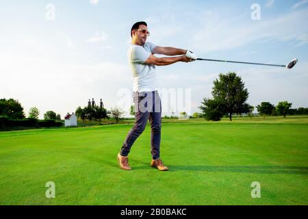 A handsome golfer is practising his swing. He is getting ready to hit the ball. Stock Photo