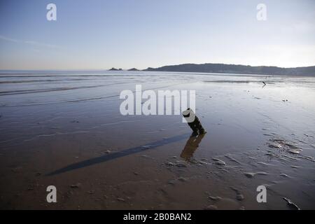 Shadows and reflections on Swansea Bay, Mumbles with lighthouse and RNLI station in distance on pier Stock Photo