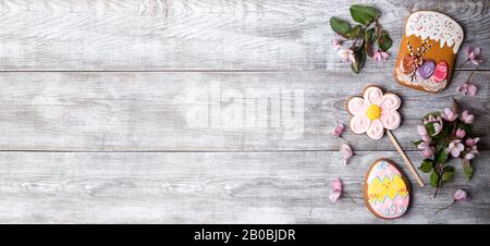 Wide festive Easter banner. Easter decorations on wooden background. Pink Apple tree branches and flowers, gingerbreads in form of Easter cake, flower Stock Photo