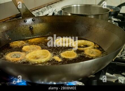 A chef deep fries Indian Pakora onion rings in hot oil over a gas stove in a restaurant kitchen Stock Photo