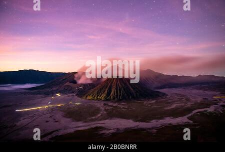 Volcanic landscape at sunrise with starry sky, smoking volcano Gunung Bromo, with Mt. Batok, Mt. Kursi, Mt. Gunung Semeru, National Park Stock Photo