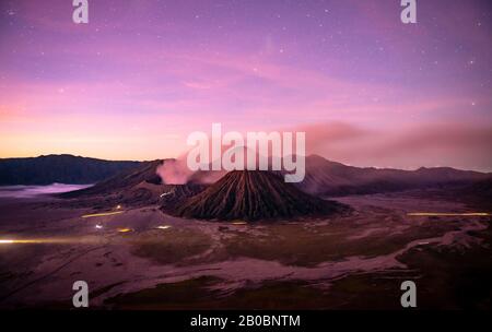 Volcanic landscape at sunrise with starry sky, smoking volcano Gunung Bromo, with Mt. Batok, Mt. Kursi, Mt. Gunung Semeru, National Park Stock Photo