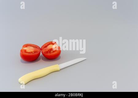 Slice tomato with yellow knife on grey background Stock Photo