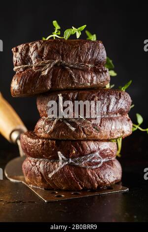 Grilled fillet steak medallions tied with string and garnished with fresh herb stacked on a metal spatula in a close up side view Stock Photo