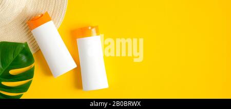 Suntan lotion bottles, female beach hat and tropical leaf isolated on yellow background. Sun protection, sunscreen cosmetic product, summer skin care Stock Photo