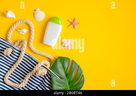 Sunscreen lotion bottle, green tropical leaves, striped beach bag, seashells on yellow background. Sun protection, suntan cosmetic product, summer ski Stock Photo
