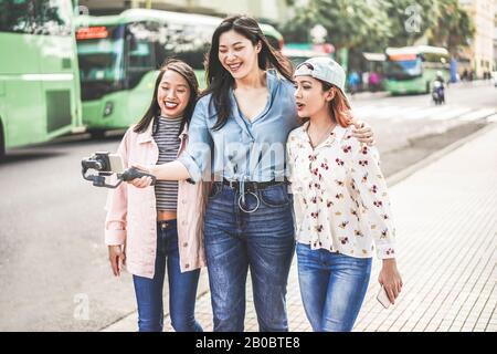 Happy asian girls making vlog video at bus station - Trendy friends blogging for social media outdoor - Technology lifestyle trends, city, casual clot Stock Photo