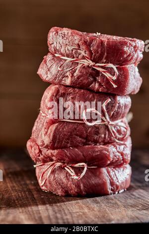 Tender thick juicy raw medallions of beef fillet steak stacked on top of one another on a wooden counter in a close up side view Stock Photo