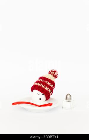 Fun breakfast concept with a boiled egg with abstract sleepy human face wearing a knitted woolen hat on white background Stock Photo