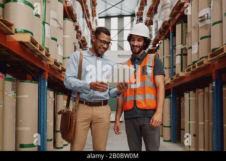 Bank manager showing loan options to warehouse manager using digital tablet in modern factory  Stock Photo
