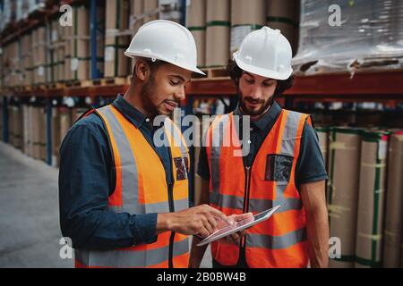 Young focused workers in warehouse discussing work on digital tablet Stock Photo