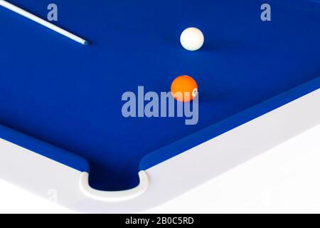 A Blue pool table with a cue, orange number five ball and the white ball Stock Photo