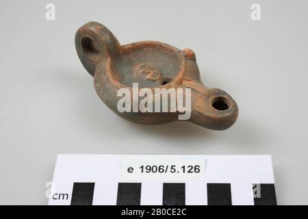 Terracotta oil lamp, decorated with mask, with ear, spout, filling hole and fire hole. Poorly readable manufacturer's mark (?). Old bonding, some pieces of the wall are missing, oil lamp, earthenware, terracotta, 9.8 x 5.5 x 3.6 cm, roman, Netherlands, Gelderland, Nijmegen, Nijmegen, Hees Stock Photo